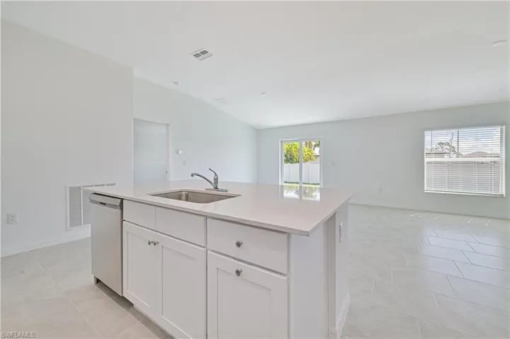 Kitchen featuring an island with sink, lofted ceiling, sink, stainless steel dishwasher, and white cabinetry