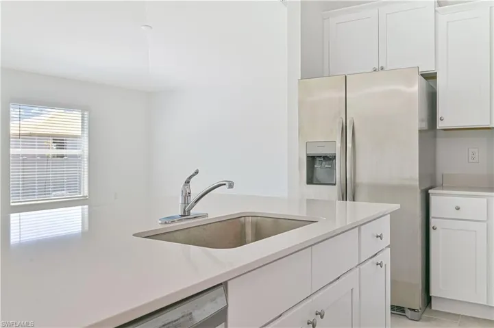 Kitchen with white cabinets, light tile patterned floors, white dishwasher, stainless steel refrigerator with ice dispenser, and sink