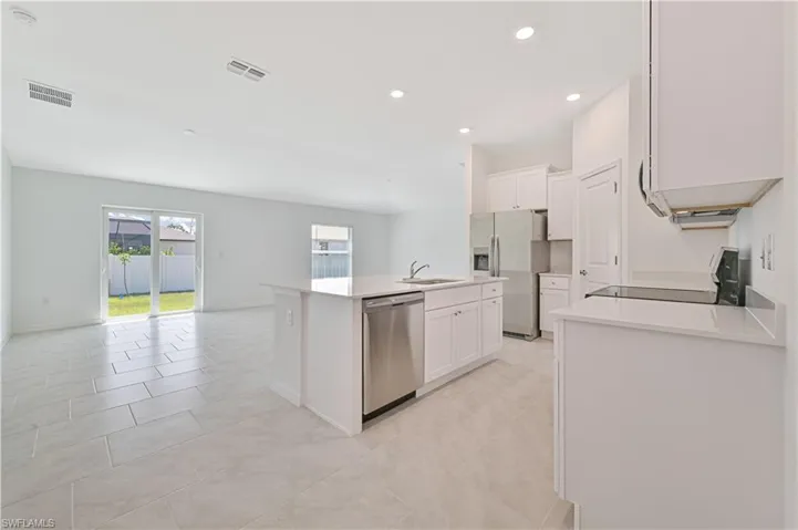 Kitchen with white cabinets, light tile patterned floors, stainless steel appliances, a kitchen island with sink, and sink