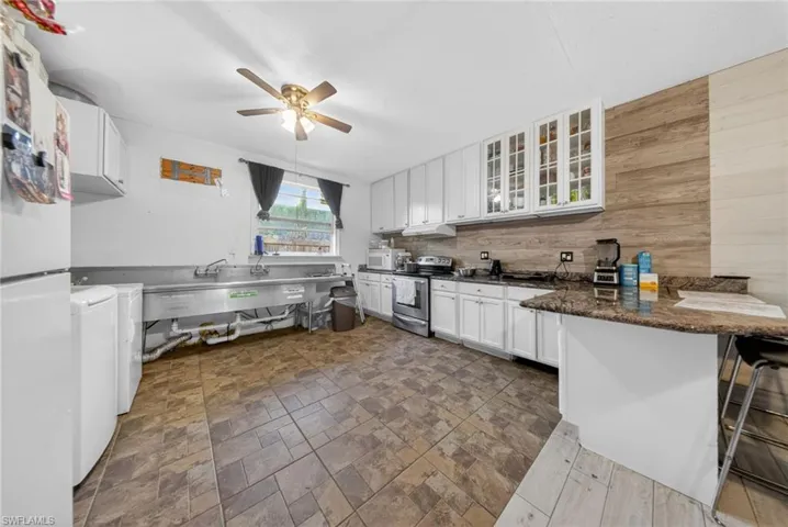 Kitchen featuring white cabinetry, white appliances, glass fronted cabinets, a peninsula, and a kitchen bar