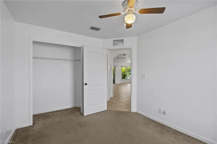 Unfurnished bedroom with carpet floors, a closet, tile patterned floors, ceiling fan, and arched walkways