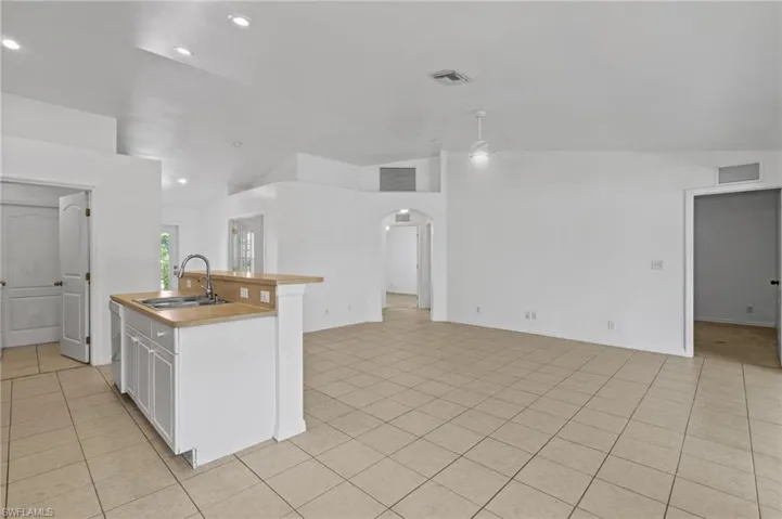 Kitchen featuring lofted ceiling, arched walkways, light tile patterned flooring, open floor plan, and light countertops