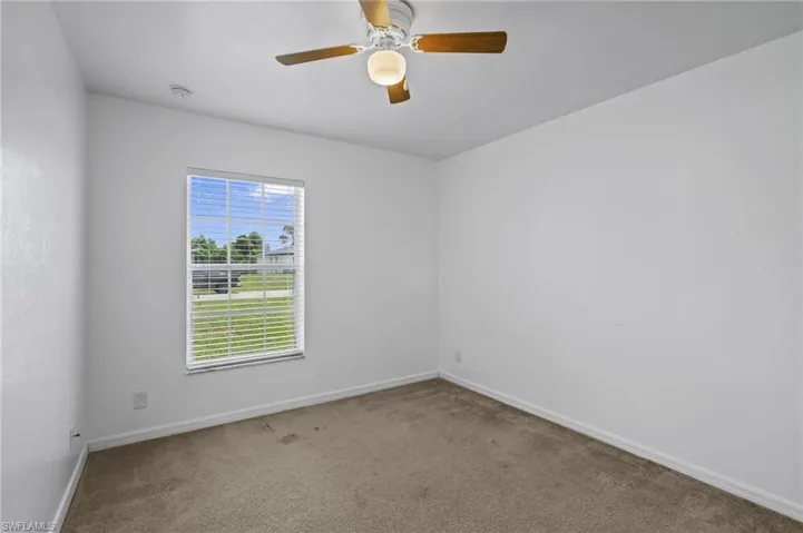 Carpeted empty room featuring a smoke detector and ceiling fan