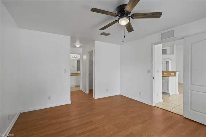 Unfurnished bedroom with light wood-style floors, ensuite bath, and ceiling fan