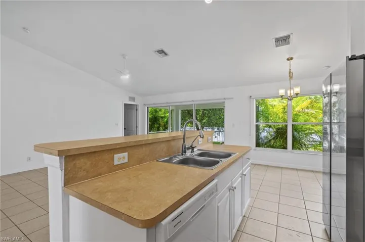 Kitchen with white dishwasher, light tile patterned floors, lofted ceiling, a kitchen island with sink, and white cabinets