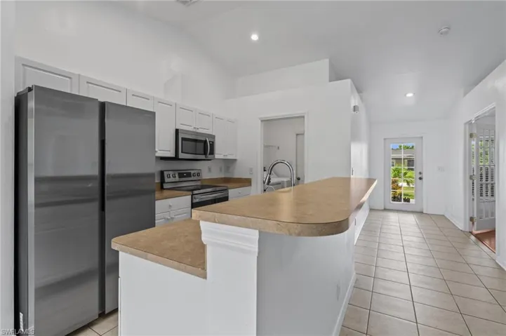 Kitchen with appliances with stainless steel finishes, light tile patterned floors, lofted ceiling, white cabinets, and light countertops