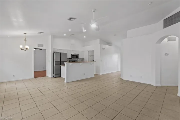 Unfurnished living room featuring a ceiling fan, arched walkways, a chandelier, high vaulted ceiling, and light tile patterned floors
