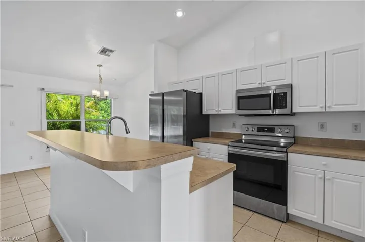 Kitchen featuring stainless steel appliances, light tile patterned floors, a center island with sink, high vaulted ceiling, and pendant lighting