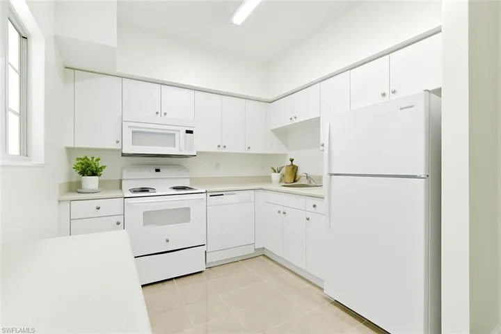 Kitchen featuring white appliances, light countertops, white cabinets, and light tile patterned flooring