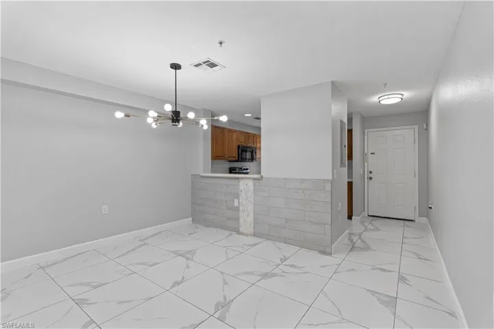 Kitchen with wood finish cabinetry, suspended lighting, light countertops, light marble finish floors, and black microwave