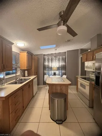 Kitchen with white appliances, a textured ceiling, ceiling fan, a kitchen island, and light countertops