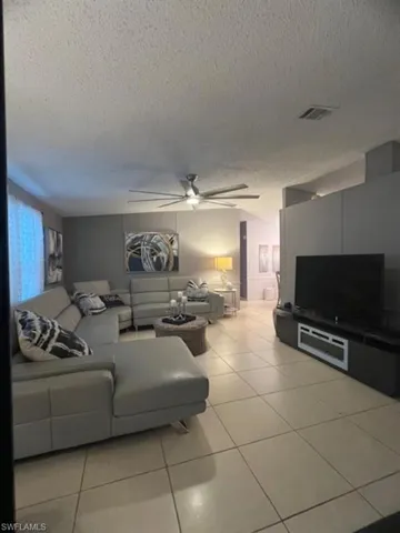 Living room with ceiling fan, a textured ceiling, and light tile patterned floors