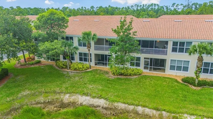 Back of property featuring a tiled roof, stucco siding, a balcony, and a lawn