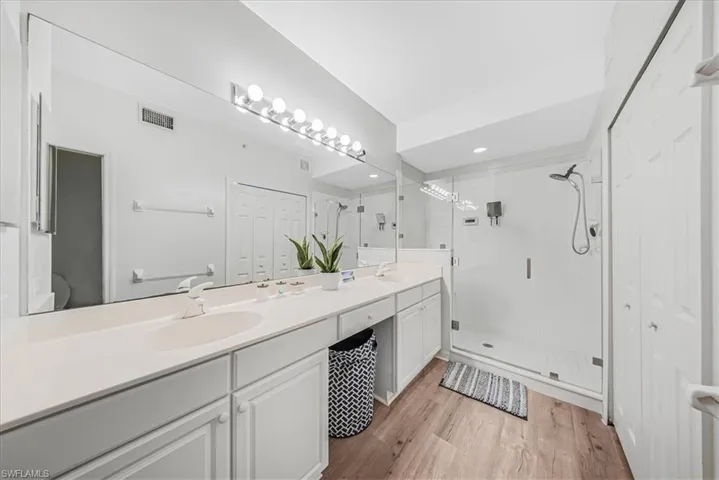 Bathroom with a closet, a shower stall, double vanity, and light wood-style flooring