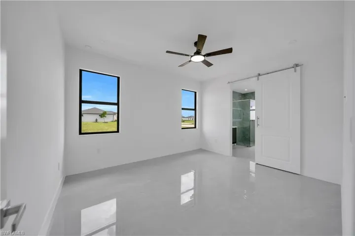 Unfurnished bedroom featuring a barn door, ensuite bathroom, and ceiling fan