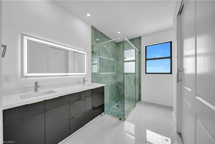 Bathroom with a marble finish shower, double vanity, and recessed lighting