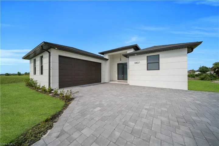 Prairie-style home featuring a front lawn, decorative driveway, an attached garage, and stucco siding
