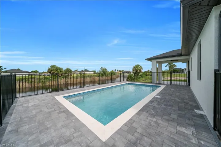 View of swimming pool with patio surround, a fenced backyard, and a water view