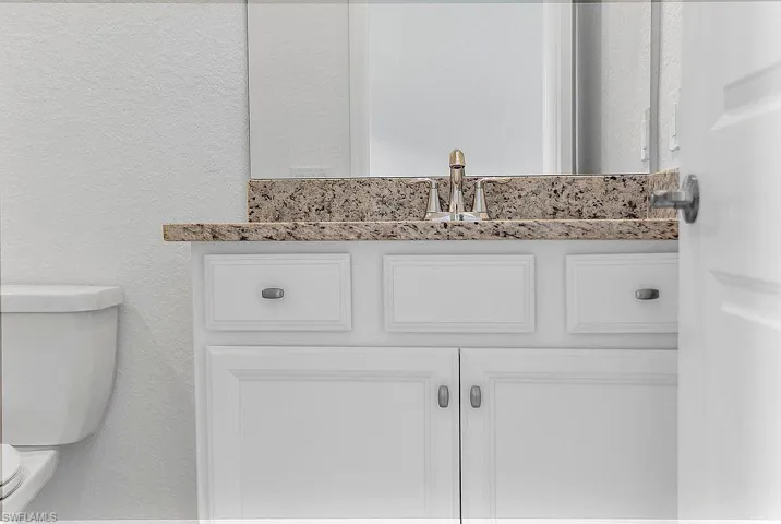 Bathroom vanity featuring a speckled countertop, white cabinetry with silver hardware, and a chrome faucet