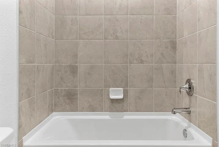 White soaking tub featuring polished chrome fixtures, integrated soap dish, and neutral-toned wall tiling