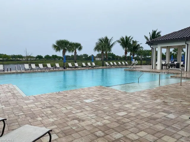 Large rectangular swimming pool surrounded by paver decking, featuring a covered cabana with tile roof and columns
