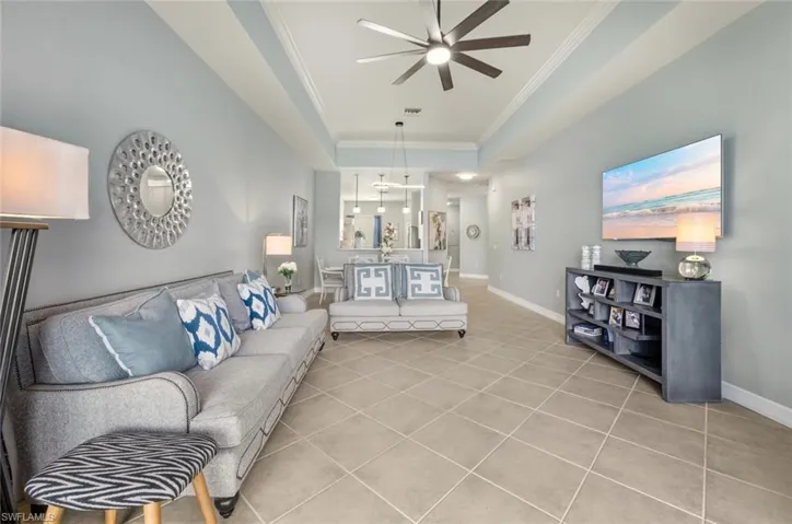 Living room with ornamental molding, light tile patterned floors, a raised ceiling, and a ceiling fan