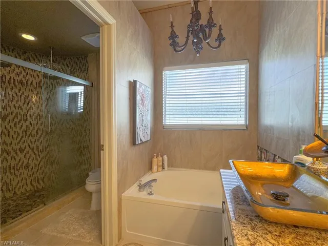 Full bathroom featuring tile flooring, plus walk in shower, an inviting chandelier, vanity, and toilet