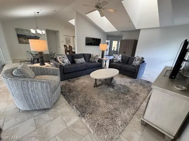 Living room with a ceiling fan, light marble finish flooring, a chandelier, and high vaulted ceiling