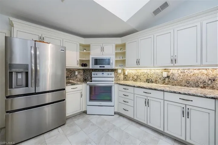 Kitchen featuring white cabinetry, white appliances, tasteful backsplash, and light stone countertops