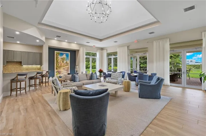 Living room featuring a healthy amount of sunlight, a tray ceiling, a notable chandelier, and light hardwood / wood-style floors