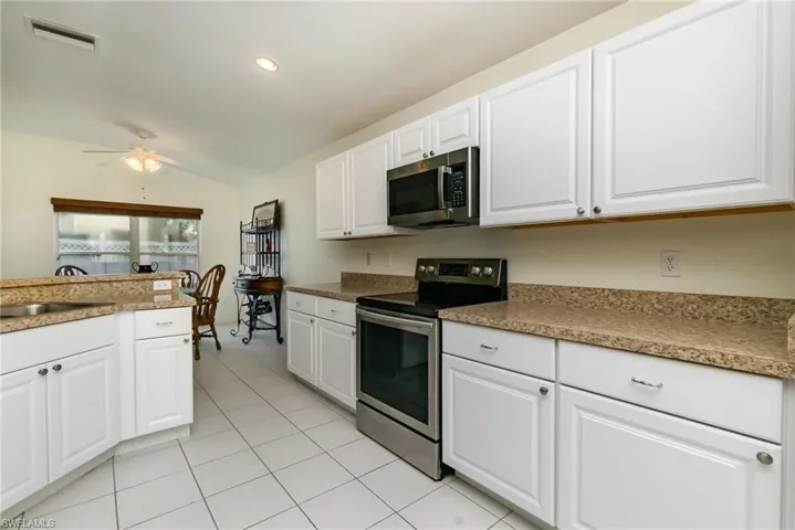 Kitchen with stainless steel appliances, lofted ceiling, light tile patterned flooring, white cabinets, and a ceiling fan