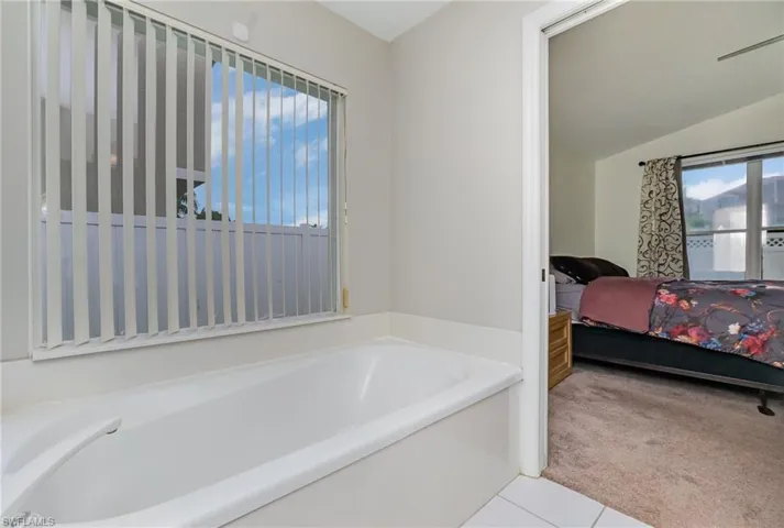 Ensuite bathroom with healthy amount of natural light, a bath, lofted ceiling, and tile patterned flooring