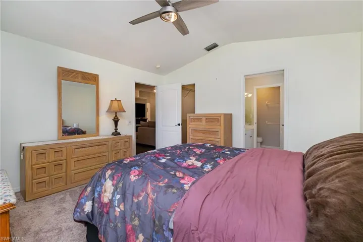 Carpeted bedroom with lofted ceiling, ensuite bathroom, and ceiling fan