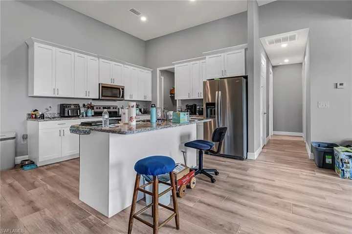 Kitchen with white cabinets, dark stone countertops, appliances with stainless steel finishes, and light hardwood / wood-style flooring