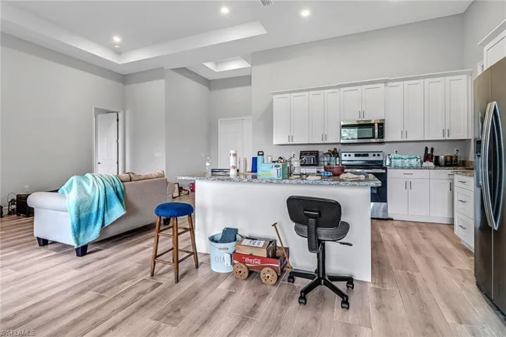 Kitchen featuring appliances with stainless steel finishes, white cabinetry, light wood-type flooring, and a center island with sink