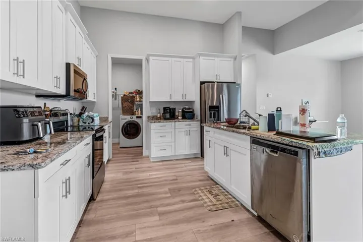 Kitchen with washer / dryer, appliances with stainless steel finishes, white cabinetry, and light hardwood / wood-style flooring