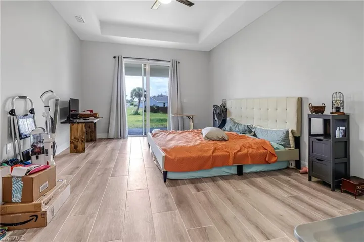 Bedroom with access to outside, ceiling fan, light wood-type flooring, and a raised ceiling