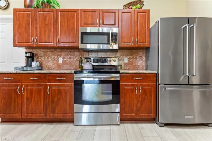 Kitchen featuring stainless steel appliances, light stone counters, tasteful backsplash, and light wood-type flooring