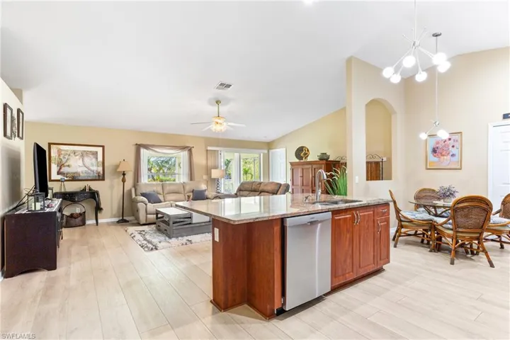 Kitchen featuring dishwasher, a sink, open floor plan, lofted ceiling, and light stone countertops