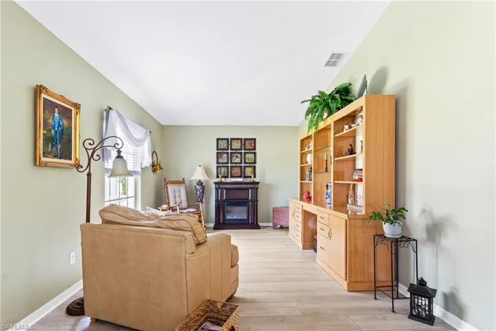 Living room featuring light wood-style floors, a glass covered fireplace, lofted ceiling, and baseboards