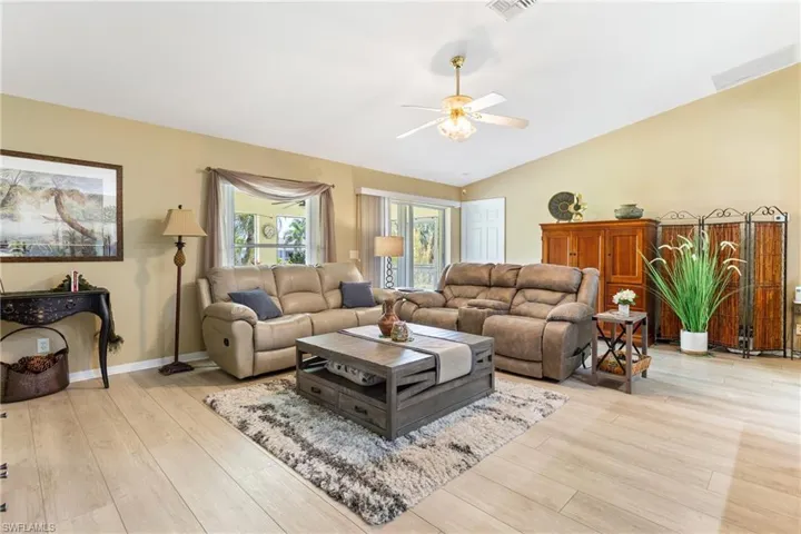 Living room with a ceiling fan, light wood finished floors, lofted ceiling, and baseboards