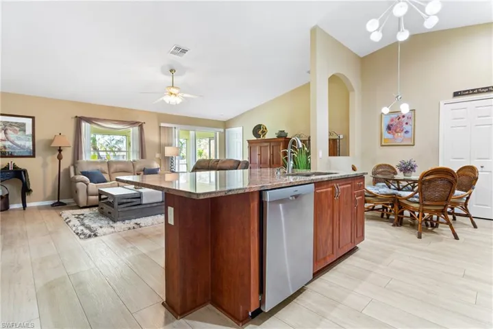 Kitchen featuring dishwasher, a sink, open floor plan, light wood finished floors, and light stone counters