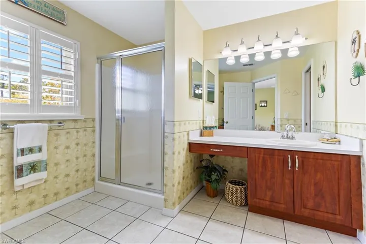 Full bathroom featuring a stall shower, a wainscoted wall, vanity, tile patterned floors, and baseboards