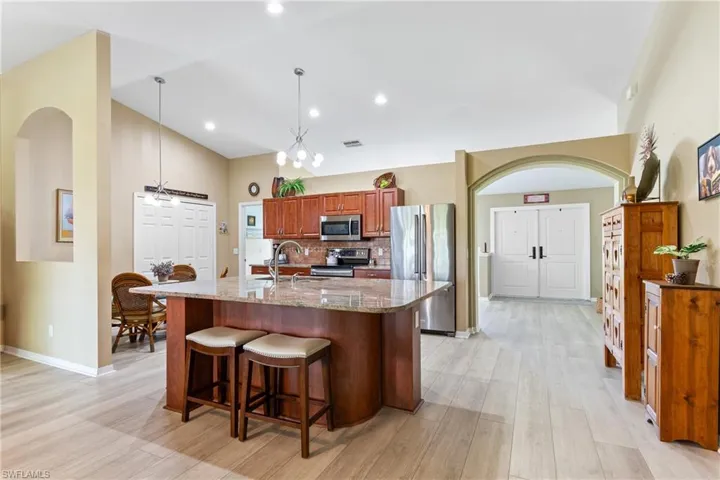 Kitchen featuring stainless steel appliances, light wood-style flooring, stone countertops, high vaulted ceiling, and a breakfast bar