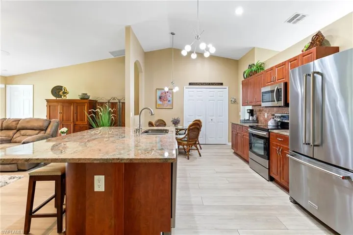 Kitchen featuring stainless steel appliances, a sink, lofted ceiling, hanging light fixtures, and light stone counters