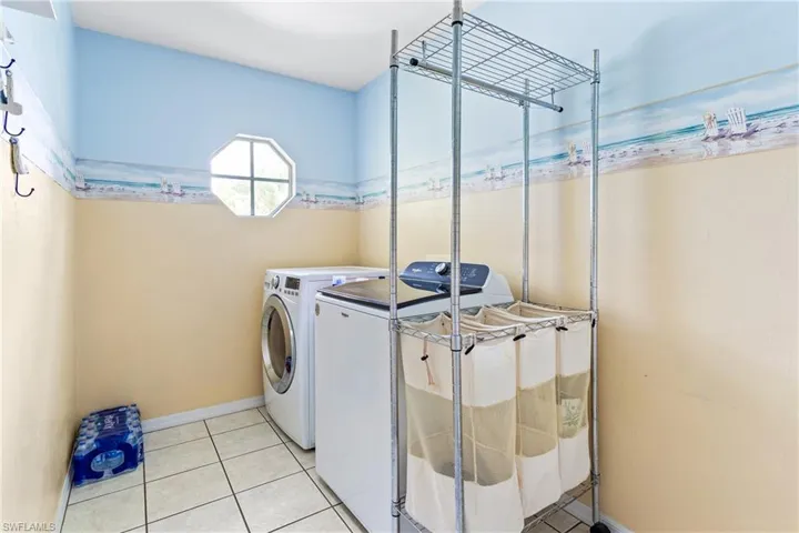 Laundry room featuring washing machine and clothes dryer, light tile patterned floors, and baseboards