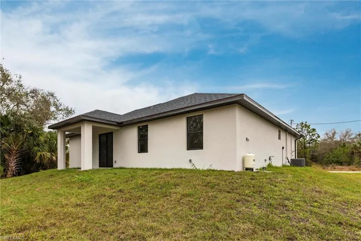 Rear view of property featuring roof with shingles, stucco siding, a yard, and central air condition unit