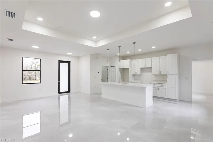 Kitchen with a raised ceiling, a center island with sink, and white cabinets