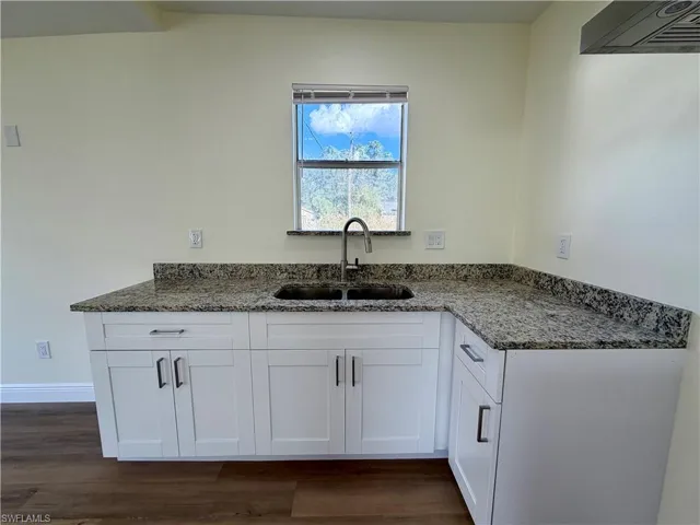 Kitchen with white cabinets, dark stone counters, exhaust hood, and dark wood finished floors