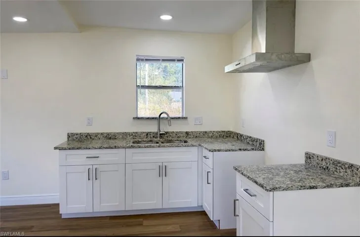Kitchen featuring wall chimney range hood, white cabinets, light stone counters, dark wood-style floors, and recessed lighting